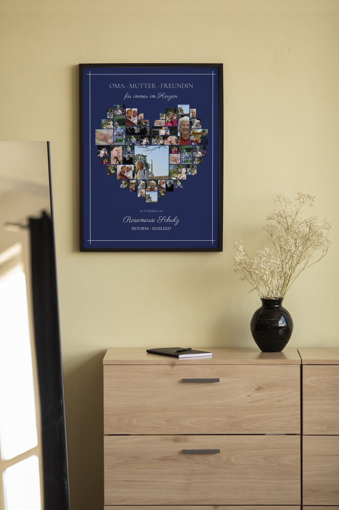 Dunkel gerahmte Gedenkcollage mit Fotoherz und Namen über einer Holzkommode neben einer Vase mit Trockenblumen